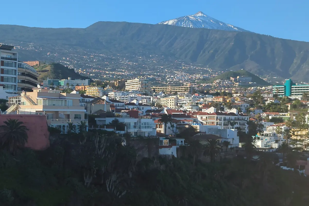 The snow-dusted summit of the Teide above a green ridge, with the white buildings of Puerto de la Cruz in the foreground